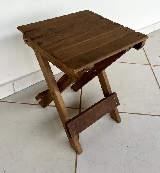 Wooden folding stool against a white wall, on a tiled floor.