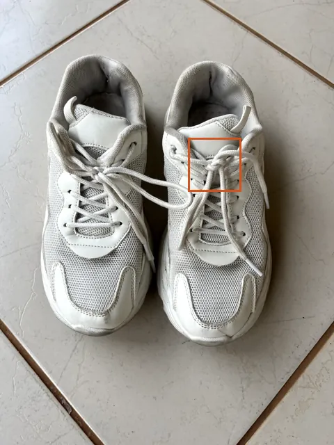 Photo of a pair of white sneakers on a light floor, with an orange square marking the laces.